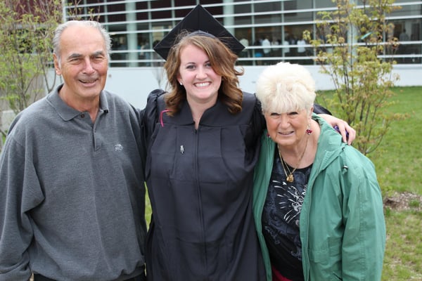 Three people standing outside; the person in the middle is wearing a cap & gown